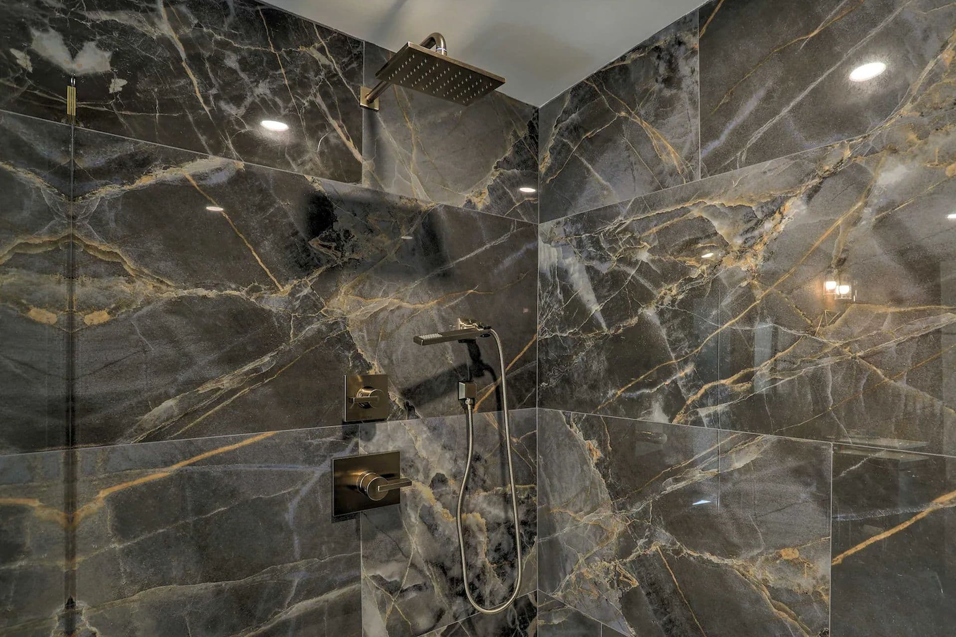 A luxurious shower with walls and floor covered in black marble with striking gold veining. A modern shower head is mounted on the wall.