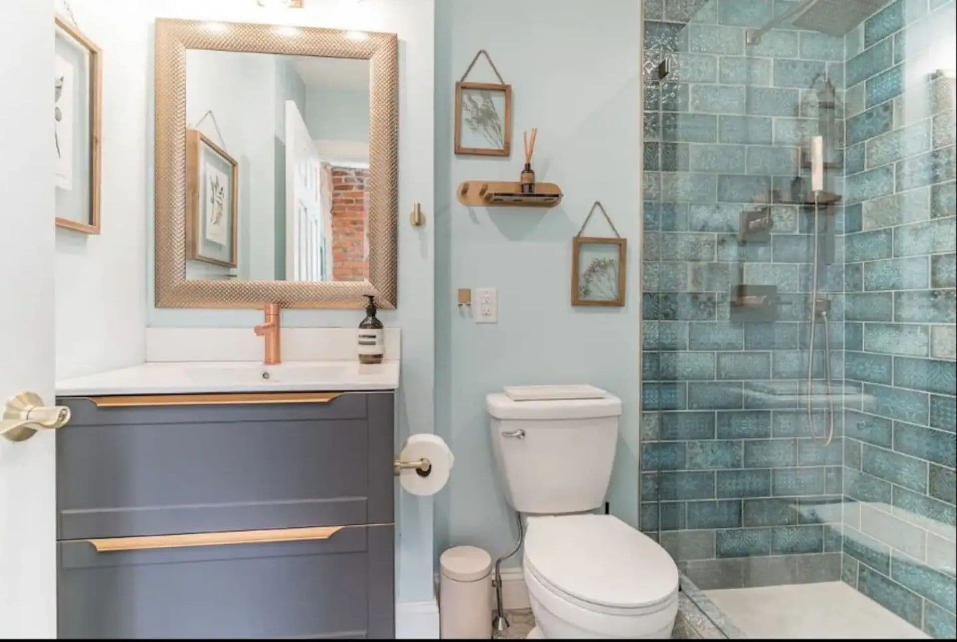 A bathroom with a gray vanity and a white toilet. A glass-enclosed shower with blue-green tiles is in the corner.
