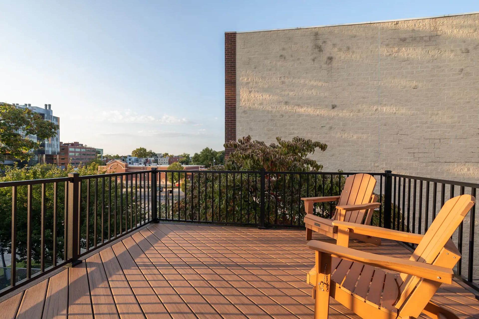 A rooftop deck with wooden Adirondack chairs and a view of the surrounding neighborhood.