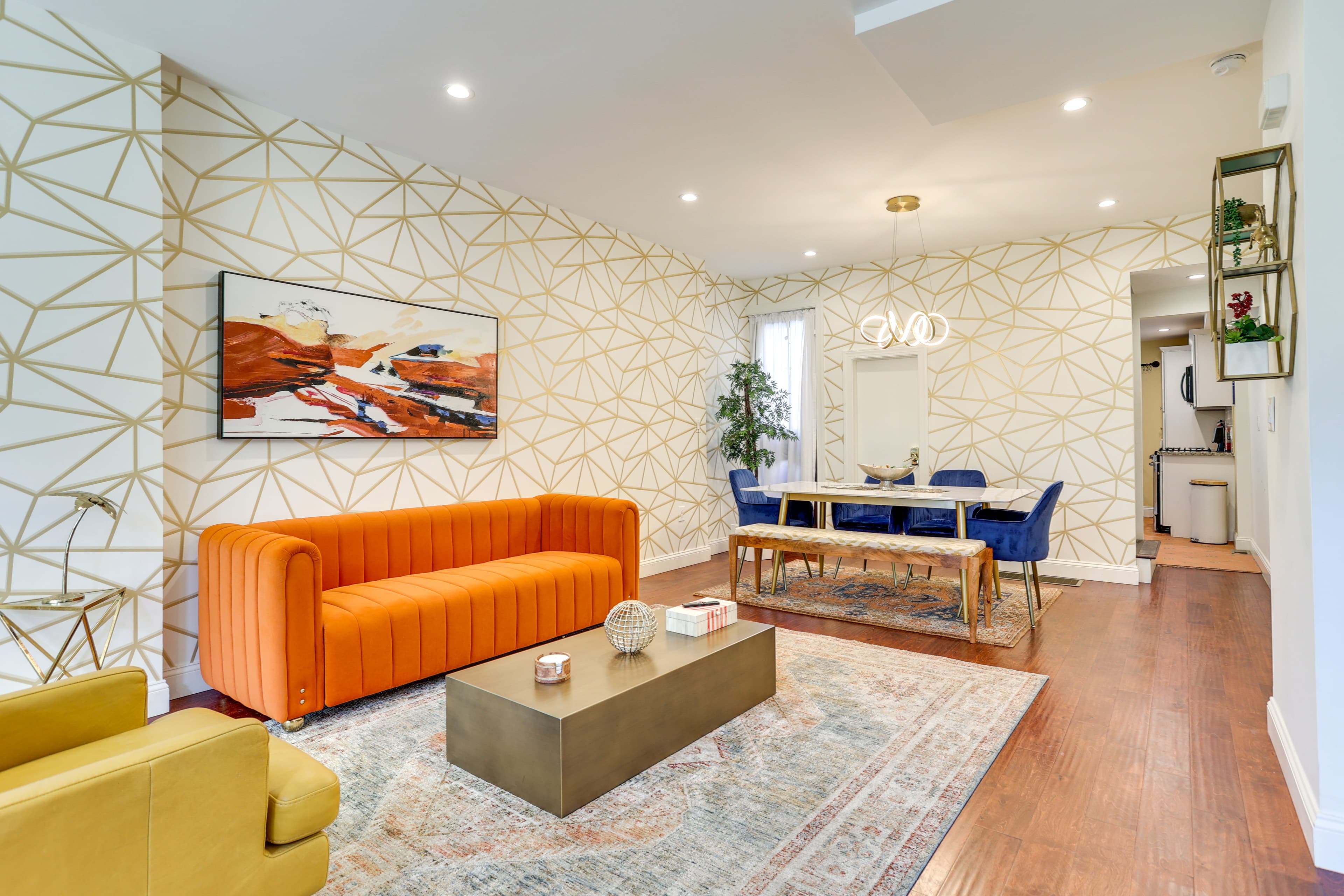 Bright living space featuring an orange sofa, geometric patterned wall, and modern dining area.