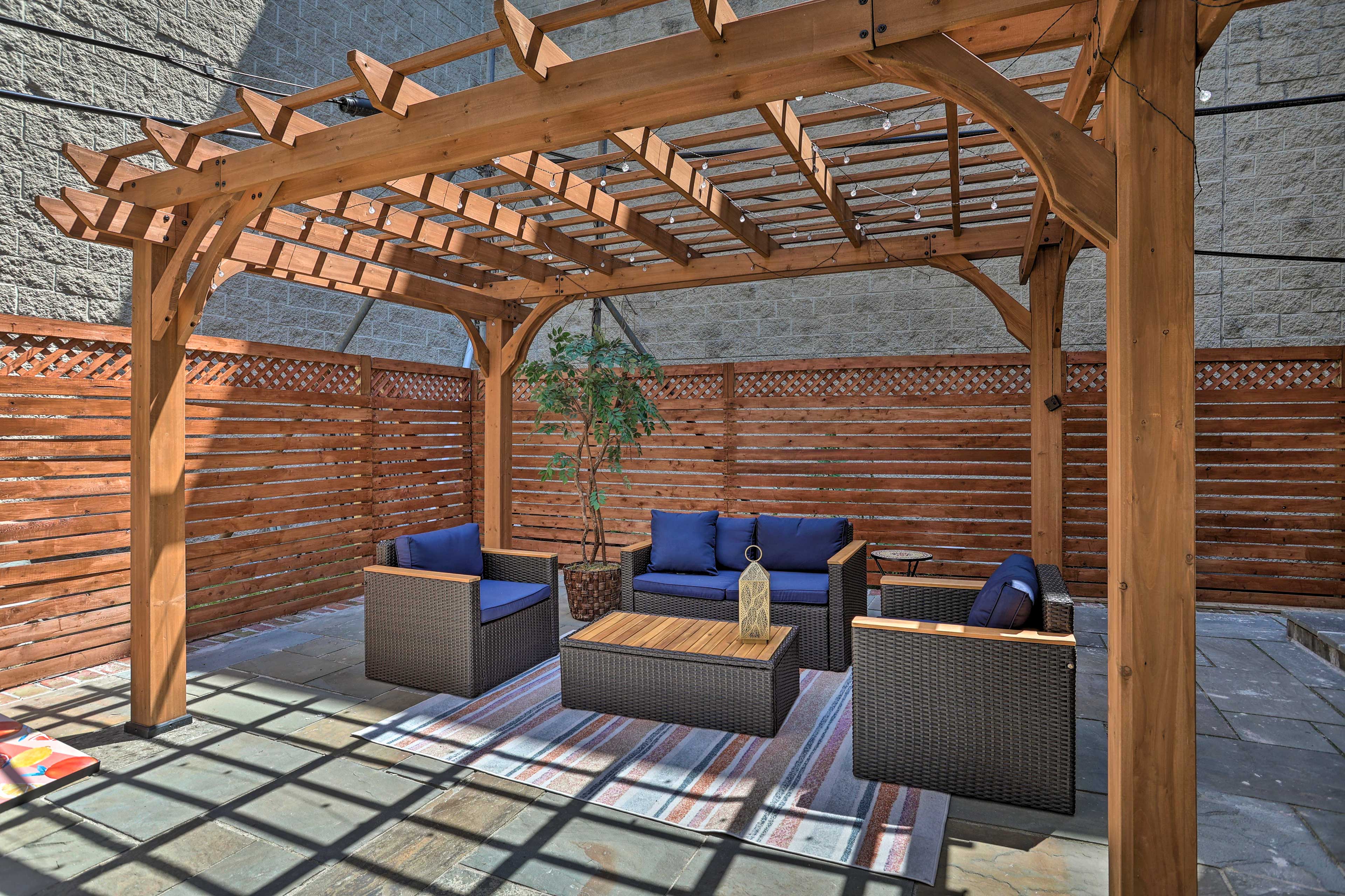 A cozy outdoor seating area with a wooden pergola and navy cushions surrounded by wooden fencing.