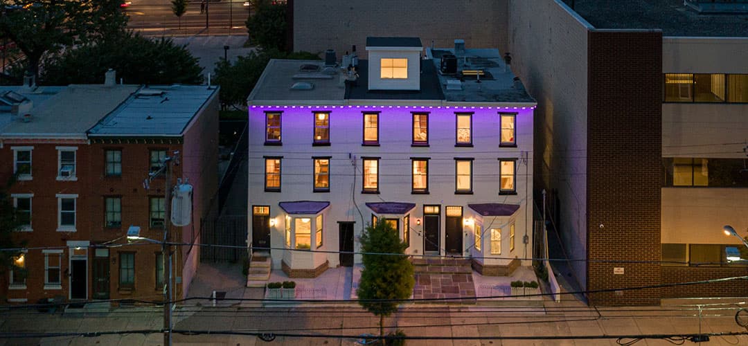 A modern three-story building with purple lighting, surrounded by other structures and power lines.