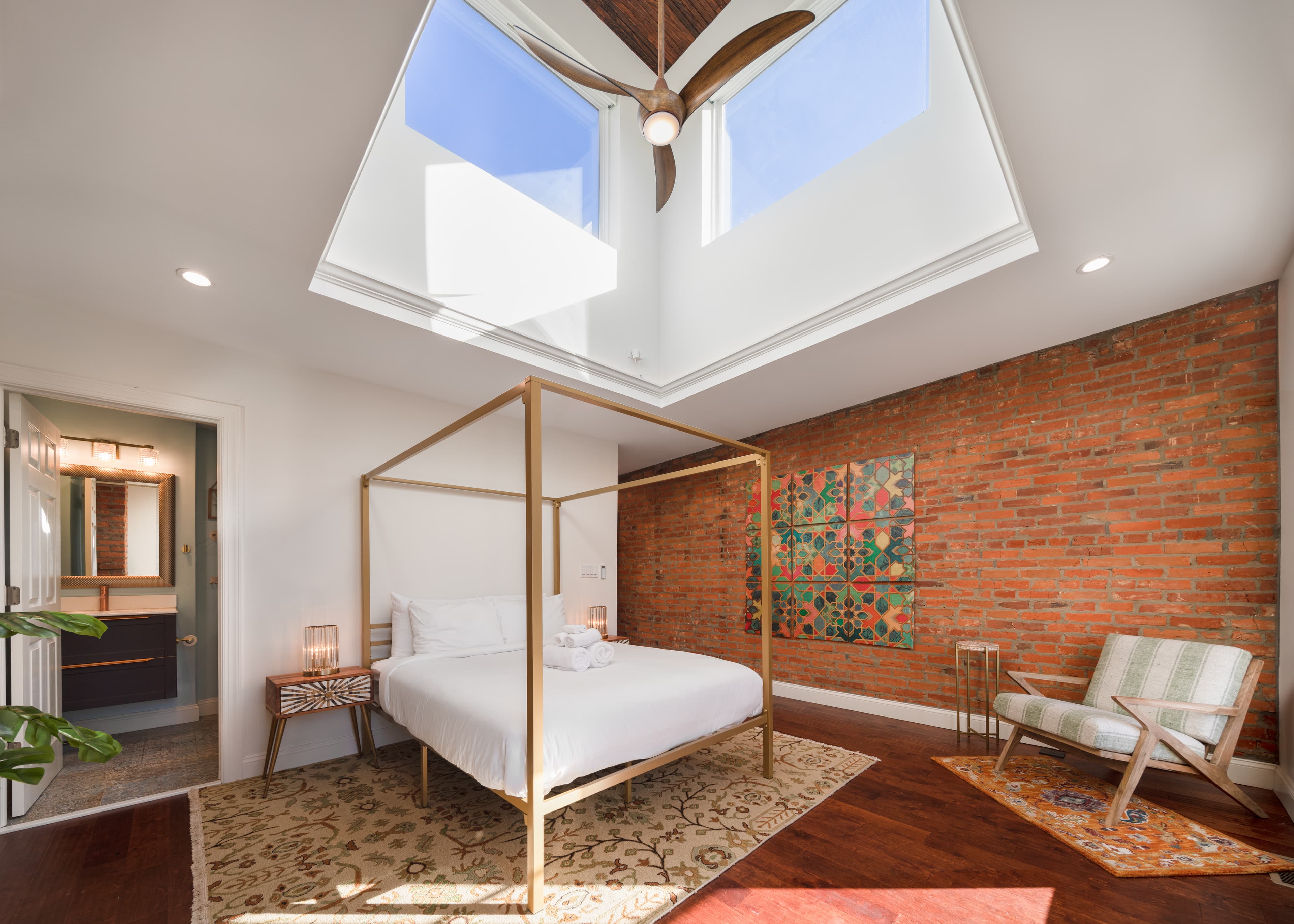 Bright bedroom featuring a four-poster bed, exposed brick wall, and large skylights.