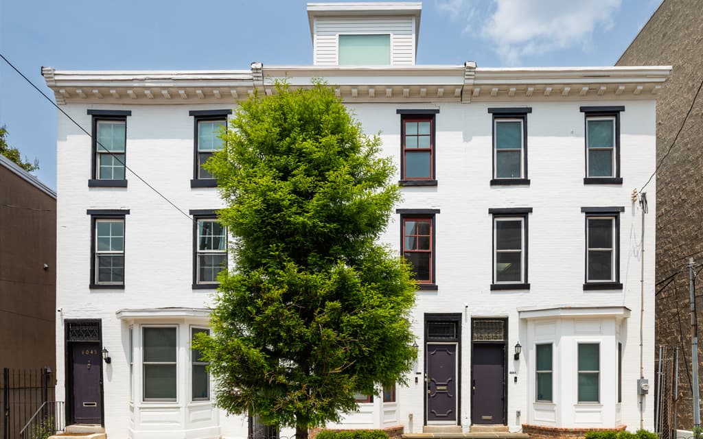 A white three-story townhouse with a central tree and various door styles.