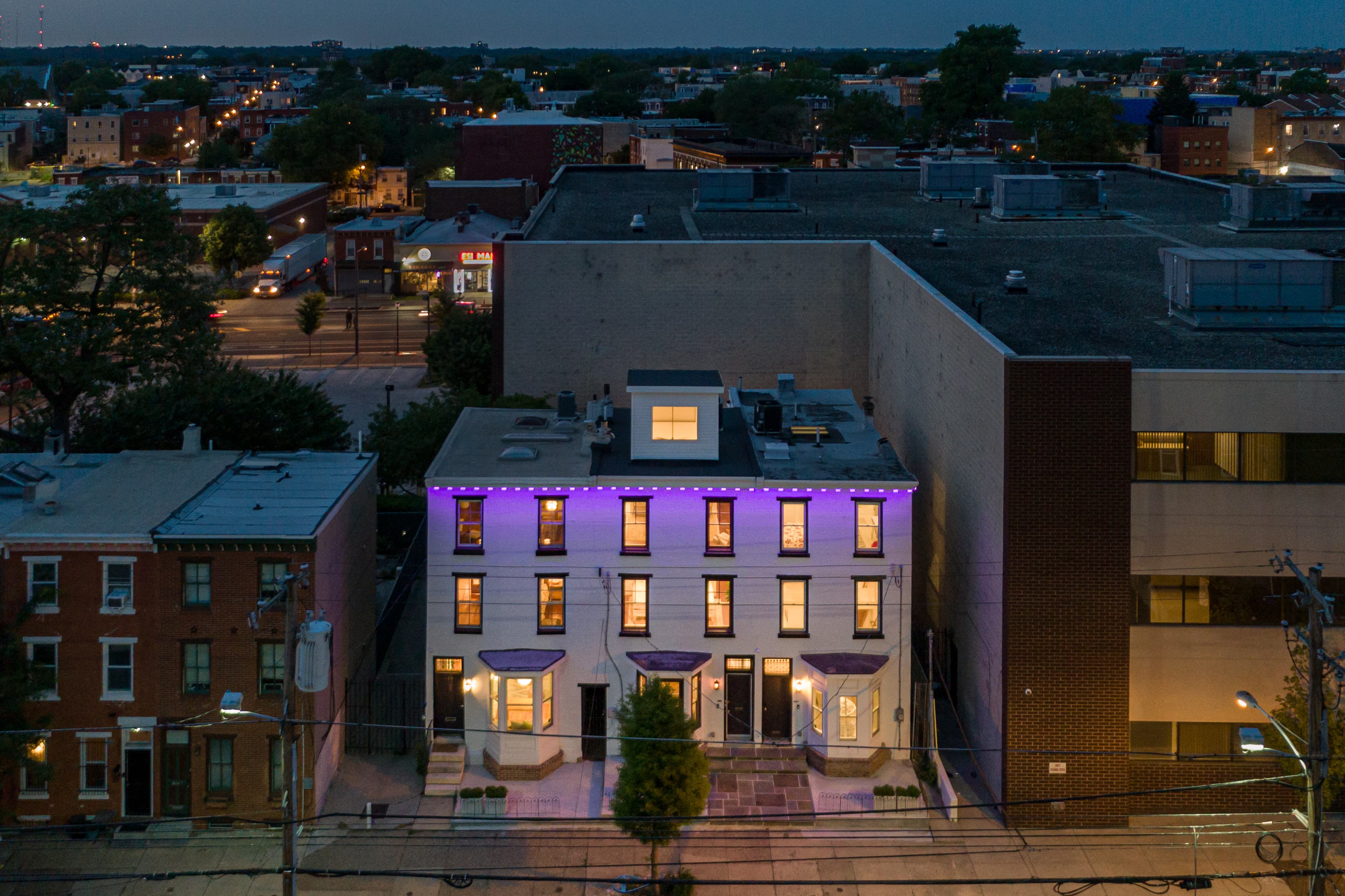 A white building with purple lights sits between two others in an urban setting at dusk.
